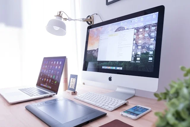 Apple Monitor Screen Show Responsive Web Design stand on Wooden Table with White color keyboard and Laptop, iPhone, Black color Touch pad, White color Table Lamp at corner green plant.
